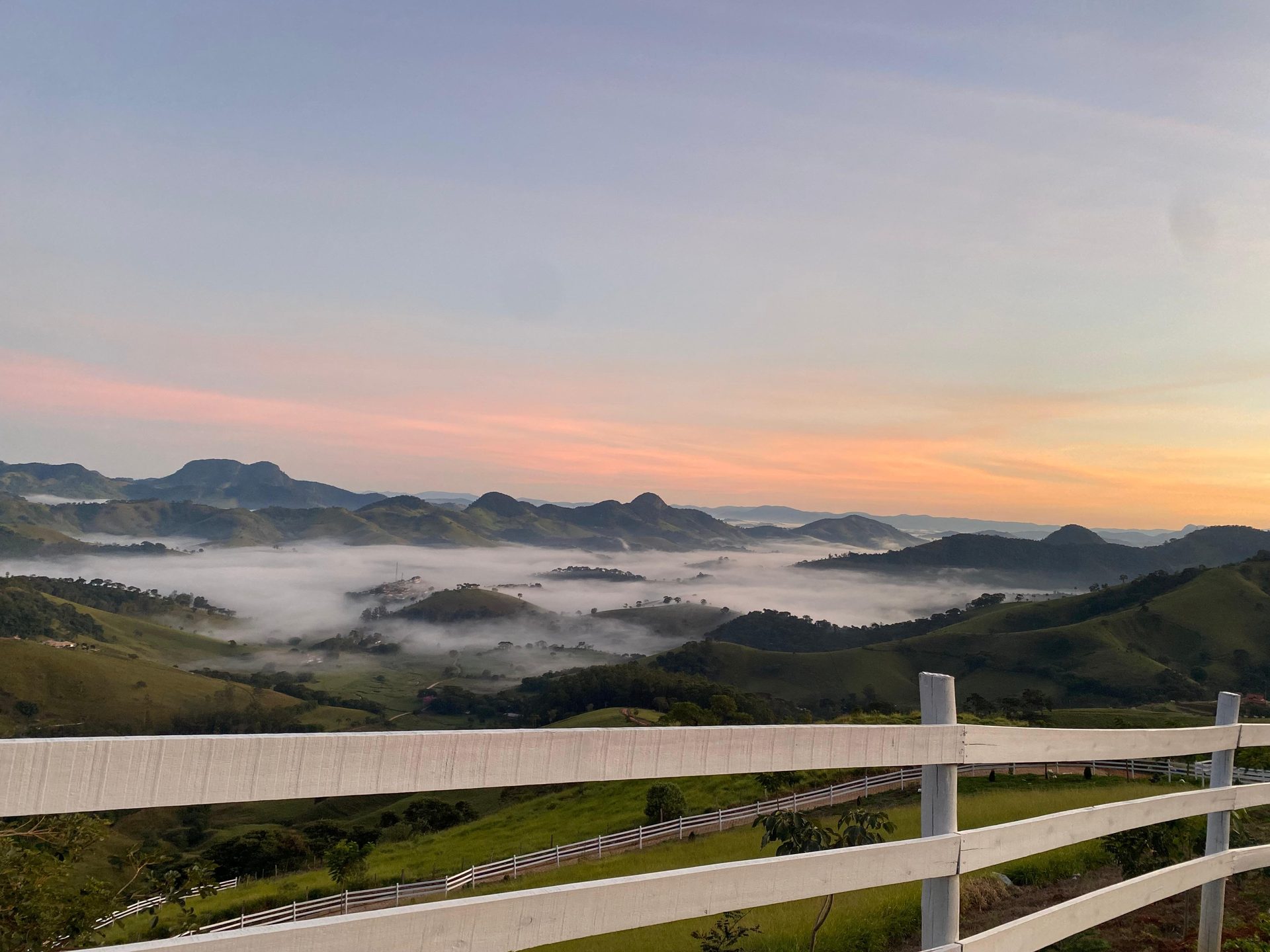 Cerca branca com mar de nuvens e céu rosado ao amanhecer